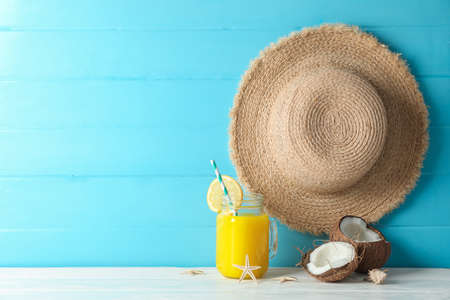 Straw hat, coconuts, fresh orange juice and starfishes on white table against color wooden...