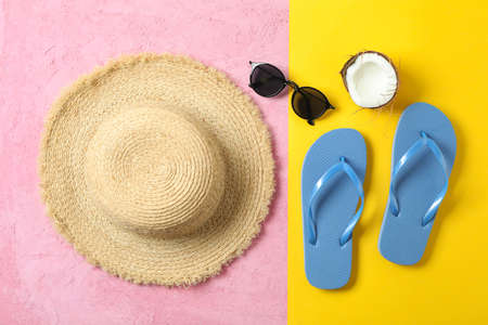 Straw hat, flip flops, sunglasses and coconut on two tone background, space for text and top view....