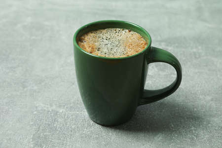Cup of coffee with frothy foam and coffee beans on grey background, space for text. Coffee time...