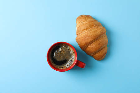 Cup of coffee with frothy foam and croissant on color background, space for text and top view. Coffee time accessoriesの写真素材