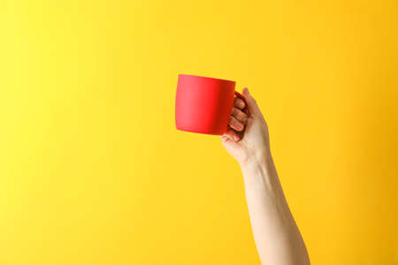 Female hand hold red cup against color background, space for textの写真素材