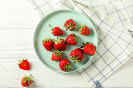 Plate with fresh strawberries and kitchen towel on white wooden background, top view and space for textの写真素材
