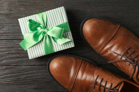 Gift box with green ribbon and brown leather shoes on wooden background, space for text and top viewの写真素材