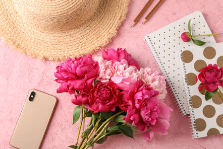 Composition with bouquet of beautiful peonies, straw hat, phone, notebooks and pencils on color background, space for text and top viewの写真素材