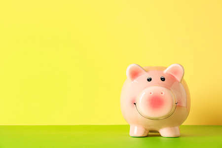Happy piggy bank on color table against yellow background, space for text. Finance, saving moneyの写真素材