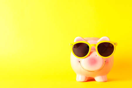 Happy piggy bank with sunglasses on yellow background, space for text. Finance, saving moneyの写真素材