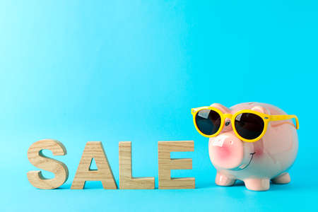 Happy piggy bank with sunglasses and inscription SALE on color background, space for text. Finance, saving moneyの写真素材