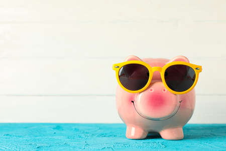 Happy piggy bank with sunglasses on color table against white wooden background, space for text. Finance, saving moneyの写真素材