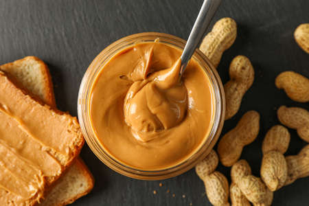 Glass jar with peanut butter and spoon, peanut, peanut butter sandwich and cutting board on wooden...