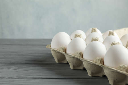 White chicken eggs in carton box on wooden table against light background, space for textの写真素材