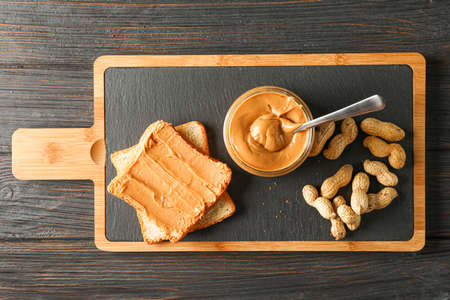 Glass jar with peanut butter and spoon, peanut, peanut butter sandwich and cutting board on wooden background, space for text and top viewの写真素材