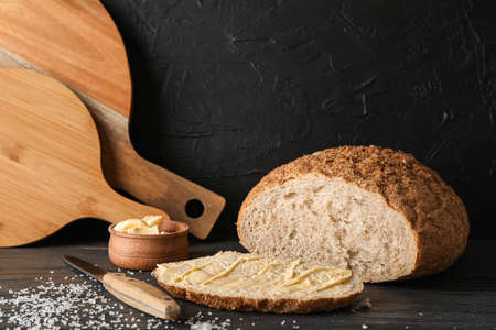 Cutting boards, bread, salt, knife and butter on wooden table against black background, space for...