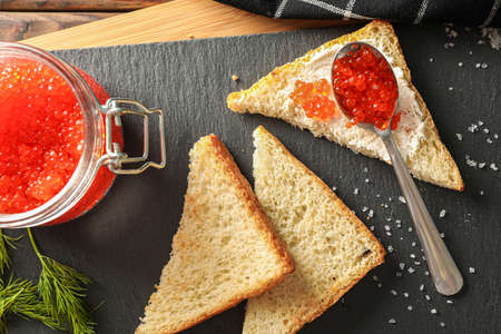 Composition with caviar in glass jar, bread, spoon, towel and cutting board, top viewの写真素材