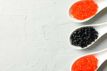 Porcelain spoons with caviar on light background, space for text