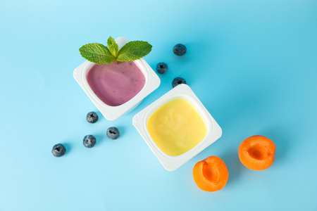 Plastic cups with yogurt and fruits on color background, space for textの写真素材