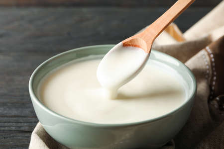 Bowl of sour cream yogurt, spoon and towel on wooden backgroundの写真素材