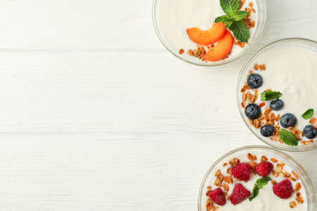 Flat lay composition with yogurt desserts and ingredients on white wooden background