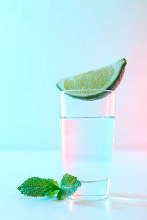 Tequila shot with lime slice and mint against white background with blue - pink lightの写真素材