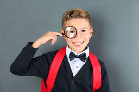 Boy in school uniform with magnifier against board, space for textの写真素材
