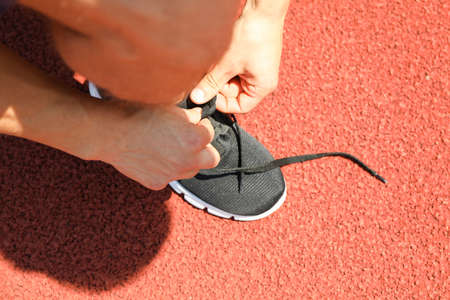 Man tying shoelaces on red athletic running track, close up
