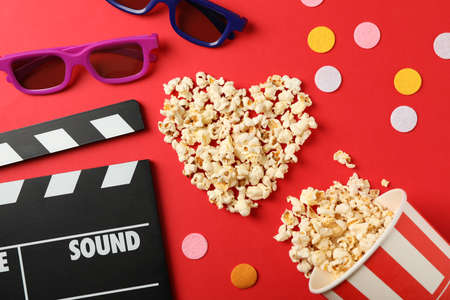 Heart laid out from popcorn, clapperboard, 3d glasses and bucket on red backgroundの写真素材
