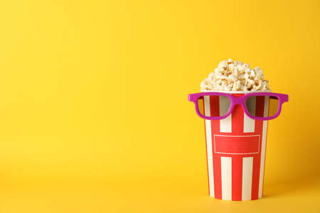 Striped bucket with popcorn and 3d glasses on yellow background, copy spaceの写真素材