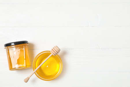 Glass jar and bowl with honey, dipper on white wooden background, space for textの写真素材