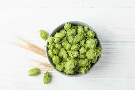 Bowl with hop and spikelets on white wooden background, space for text