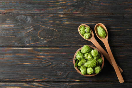 Wooden bowl and spoons with hop on wood background, copy space