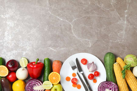 Vegetables, fruits, plate and cutlery on grey background, copy space