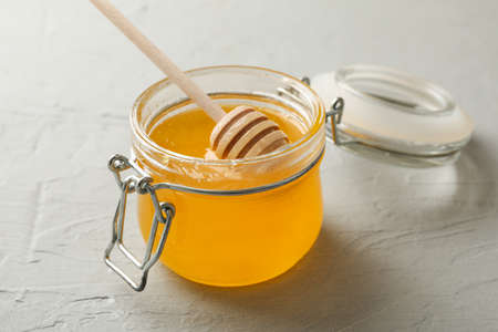 Glass jar with honey and dipper on white background, closeup
