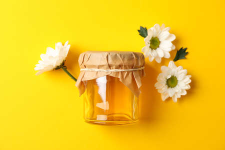 Glass jar with honey and chamomile on yellow background, space for textの写真素材