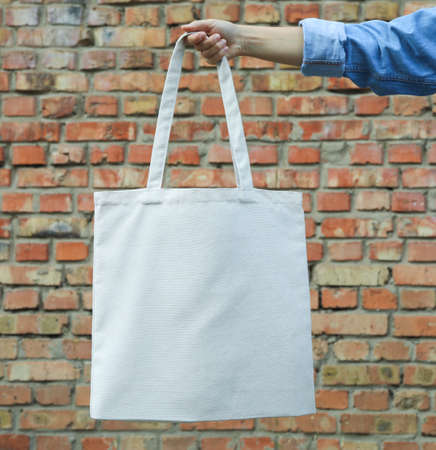 Female hand holding tote bag against brick wall, empty space