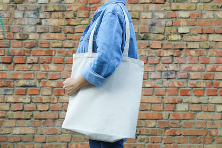 Young woman holding tote bag against brick wall, empty space