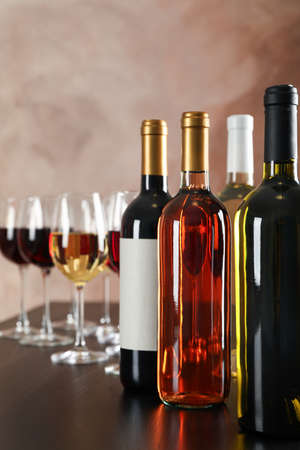 Bottles and glasses with wine against brown background, copy space