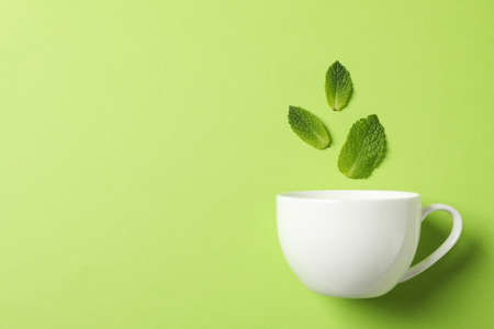 White cup and leaves on green background, space for text