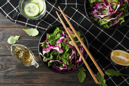 Black bowls with salad, chopsticks and towel on wooden background, top viewの写真素材