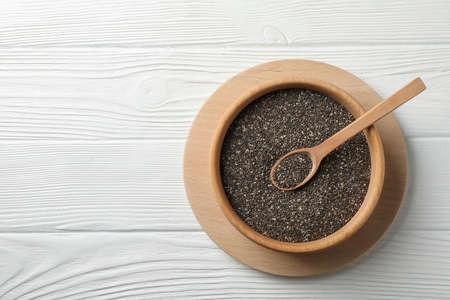 Wooden bowl with chia and spoon on white wooden background, top view