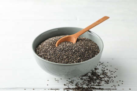 Chia seeds, wood spoon and bowl on white wooden background, copy space