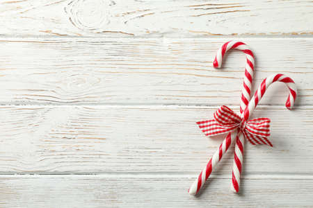 Sweet candy canes with bows on white wooden background, space for text