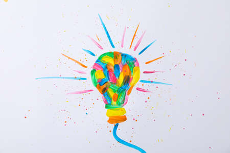 Multicolored light bulb and paint splatters on white background, space for textの写真素材