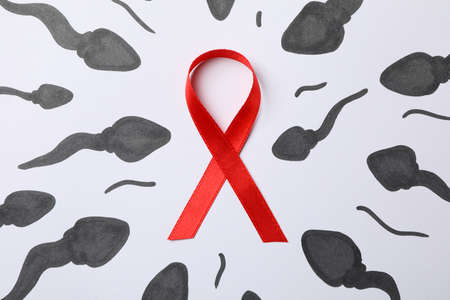 Red awareness ribbon and sperm cells on white background, close up