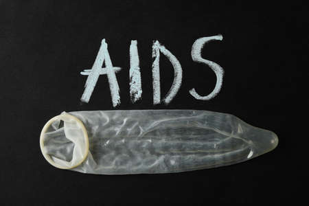 Condom and inscription AIDS on black background, space for text