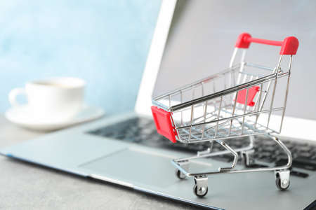 Shopping cart, cup of coffee and laptop on grey background, copy space