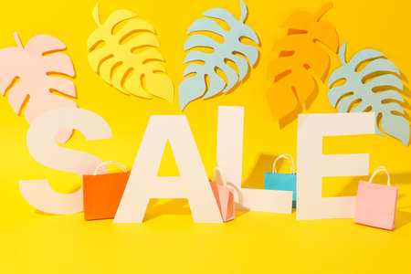 SALE, paper bags and palm leaves on yellow background, copy space