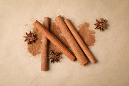 Cinnamon sticks, powder and anise stars on beige or cardboard background, top view