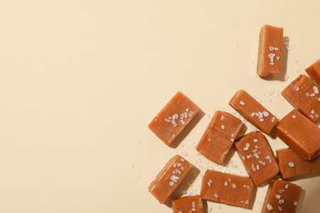 Salted caramel candies on beige background, space for text