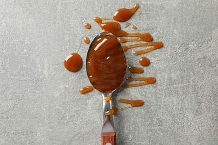 Spoon with caramel on grey background, space for textの写真素材