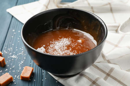 Bowl with salted caramel and candies on wooden background, close upの写真素材