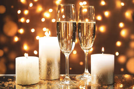 Champagne glasses and candles against blurred lights background, space for textの写真素材